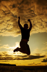 Silhouette of a young man in a jump against the backdrop of the setting sun and sky. The concept of happiness, activity, freedom, health. Man of dense build in a t-shirt and shorts. Place for text.