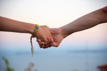 Two hands, male and female, holding each other tightly, on a blurred light background. On the female hand is a bright bracelet.