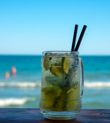A steamed glass of Mojito on the bar with two black tubes.Against the sea and blue sky.