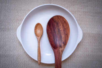 White plate with a wooden spoon on a brown tablecloth, suitable for advertising or graphic work, top view