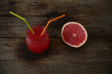 glass of fresh red grapefruit juice and sliced ​​half a grapefruit on a rustic wooden background. With copy space for text. Healthy food, diet concept, detox.