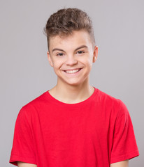Close up emotional portrait of caucasian teen boy. Handsome smiling guy. Funny cut teenager on gray background. Child looking at camera.