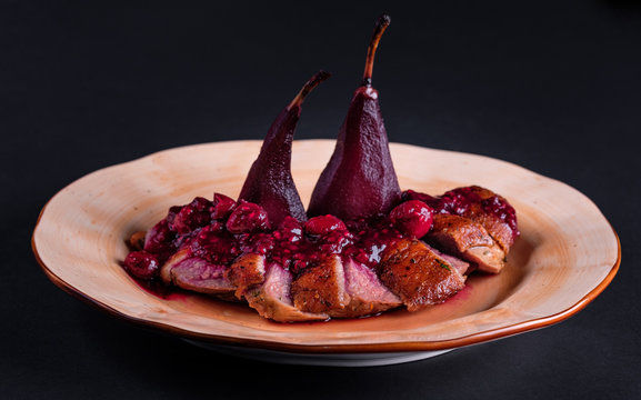 Exclusive restaurant meals. Sliced duck fillet confit with baked pear and cherry sauce served on plate on black table background. Christmas or thanksgiving fest food. Copyspace