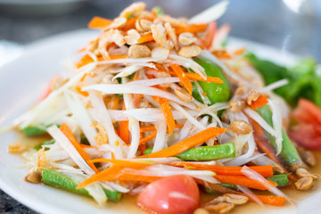 Papaya salad on a white plate on a wooden table
