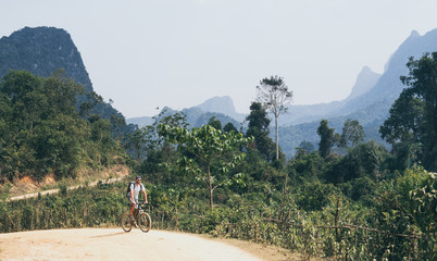 Young Caucasian man riding a mountain bicycle uphill in Muang Ngoi village, Laos