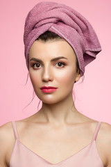 Beauty Woman face with hands. Beautiful Portrait Spa model Girl with Perfect Fresh Clean Skin. Female looking at camera and smiling. Youth and Skin Care Concept. Pink towel on the head, space for text