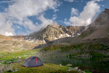 Tourist tent stands next to a high-mountain lake on the background of Mount Dzhalkaush, height 3283, Teberda, Karachay-Cherkessia, Russia