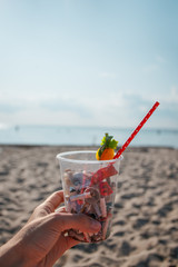 Hand holding cocktail with garbage on background of clean beach, ocean waves. Plastic ocean pollution, environmental crisis. Say no plastic. Single-use plastic waste