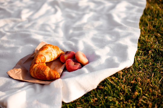 Croissants and fig peaches on a white plaid lie on the grass. Picnic on a sunny day.