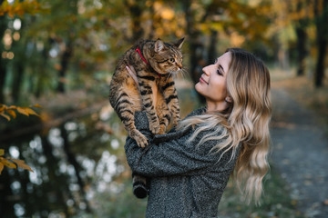 girl and a cat in the autumn park.a woman in a brown sweater walking with her gray cat in an autumn park