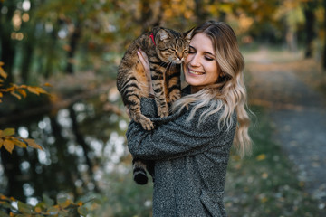girl and a cat in the autumn park.a woman in a brown sweater walking with her gray cat in an autumn park