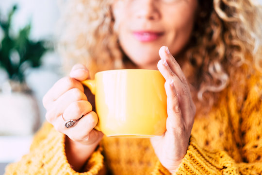 Close up on cup with tea or coffe drink inside and beautiful defocused woman in background - concept of relax and healthy lifestyle with nice people - yellow colors mood