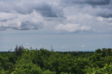 Dark cloudy rain sky before rainy above the roof building and green trees in the city.