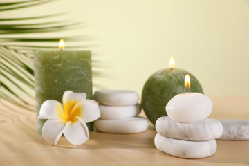 Fototapeta na wymiar Composition of spa stones and burning candles with flower on wooden table against light green background