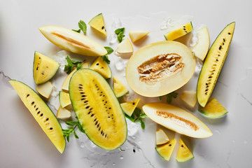 Top view of cut delicious exotic yellow watermelon and melon with ice and mint on marble surface