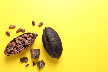 Cocoa pods with beans and chocolate pieces on yellow background, flat lay. Space for text