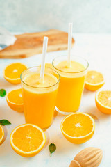 Top view of orange smoothie and orange fruits with green leaves on white background.