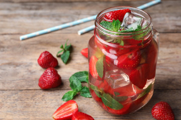 Mason jar of refreshing drink with strawberry and mint on wooden table, space for text