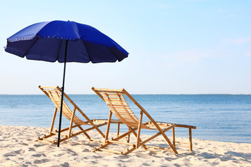 Empty wooden sunbeds and umbrella on sandy shore. Beach accessories