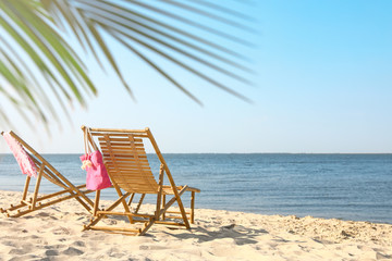 Empty wooden sunbeds and beach accessories on sandy shore