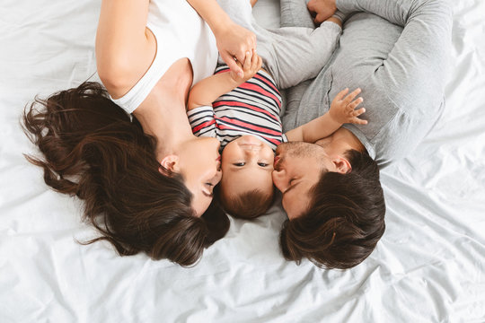 Happy parents kissing cute baby son in bed