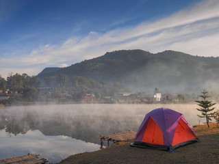 Lake view morning of a camping tent on the bank around with soft mist, reservoir, mountain and cloudy sky background, Ban Rak Thai Reservoir, Mae Hong Son, northern of Thailand.