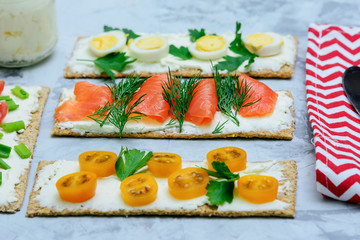 Little snacks with different ingredients. Crispy bread sandwiches with curd cheese, trout, tomato and dill. Light summer snack.