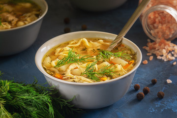 Chicken Noodle Remedy Soup Bowl Closeup Dinner. Healthy Meat Broth in White Dish with Spoon. Vegetable Poultry Bouillon with Dill Branch. Pink Salt Scattered on Kitchen Table. Warm Homemade Lunch
