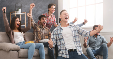Excited friends having fun by watching football match at home