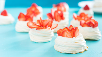 Obraz na płótnie Canvas Beautiful pavlova cakes with strawberries on a blue background. Selective focus. Tasty sweet breackfast. Wedding morning. Meringue with cream.