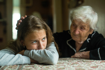 Old lady grandma comforting a crying little girl granddaughter.