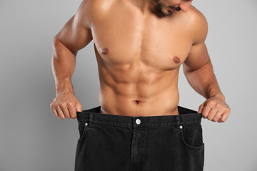 Young man with slim body in old big size jeans on grey background, closeup view