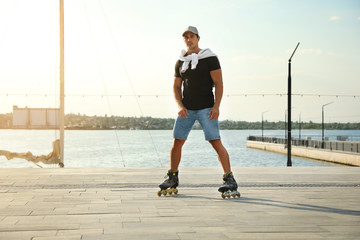 Handsome young man roller skating on pier near river, space for text