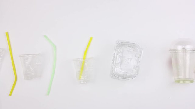 different used dirty plastic disposable tableware and garbage moves on white background, bottles cups bags containers, stopmotion animation, big ecological pollution problem