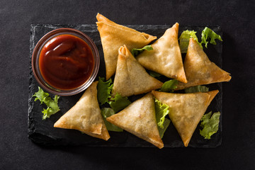 Samsa or samosas with meat and vegetables on black background. Traditional Indian food. Top view.