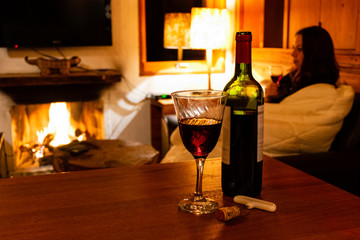 Blurred background woman holding glass of wine. Foreground bottle of wine and glass.