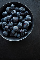 Fresh blueberries in a dark ceramic bowl on a black background, top view, close-up
