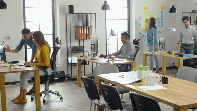 Female Specialist Works on Desktop Computer, Project Manager Stands Beside and gives Advice on Optimizing Workflow for Customer Experience Management. Modern Office with Diverse Team of Professionals