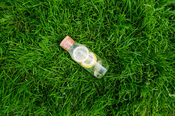 Lemonade with lemon and ginger in a glass bottle on green grass. Delicious refreshing summer drink.