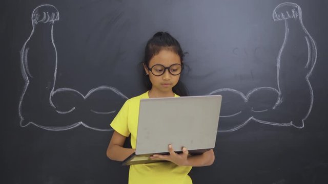 Female elementary school student using a laptop computer with strong hands or chalk muscles on the blackboard in the classroom at school. Shot in 4k resolution