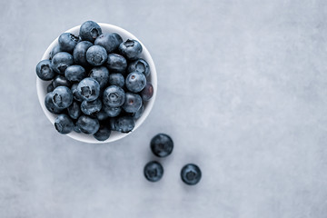 Fresh blueberries in a white bowl on a gray background. Top view.