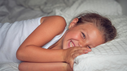 Authentic shot of cute smiling little girl daughter and young mother are having fun to stay together after waking up in a bed with white sheet in the morning.