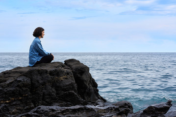Fototapeta na wymiar Woman on a rock looks towards the ocean contemplating it.