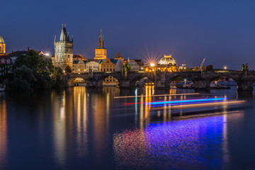 Fototapeta na wymiar Old Town tower and historic stone bridge with lighting and reflections from the ship on the water. Prague with Charles Bridge at night. Panoramic view over the Vltava