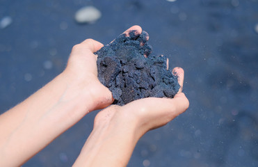 Female hands with volcanic black sand on ocean beach background