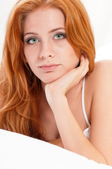 Obraz premium Beautiful young woman in bed, looking at camera. Closeup portrait of attractive Girl with red hair and green eyes - indoors.