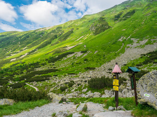 Trail signpost at footpath trail in mountain valley Smutna dolina with rock boulders, scrub pine and green mountain peaks. Western Tatras mountains, Rohace Slovakia, Summer blue sky white clouds © Kristyna