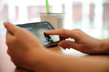 Female hand with smartphone trading stock online in coffee shop , Business concept