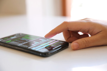 Female hand with smartphone trading stock online in coffee shop , Business concept