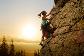 Beautiful Woman Climbing on the Rock at Foggy Sunset in the Mountains. Adventure and Extreme Sport Concept - obrazy, fototapety, plakaty